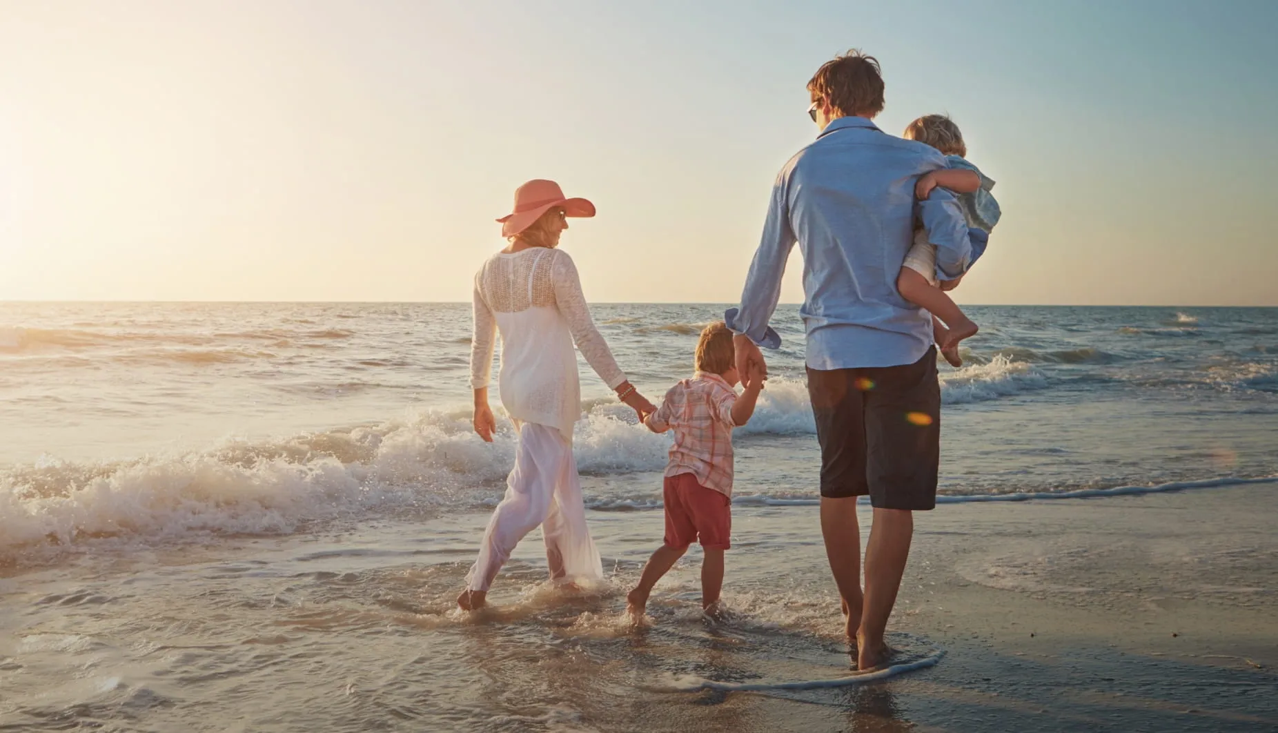 Familia con 2 niños pequeños caminando por la arena de la playa